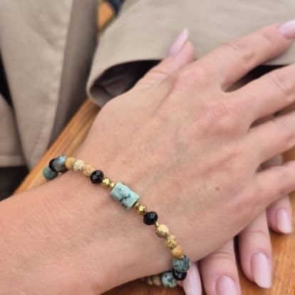 Close-up of a beaded bracelet worn on a persons wrist, featuring black, gold, and green gemstone beads