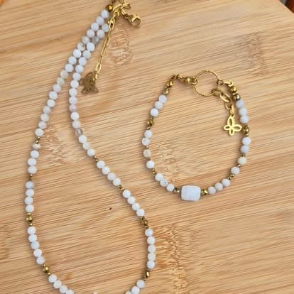 Two pieces of jewelry with white beads and gold metal accents on a wooden surface