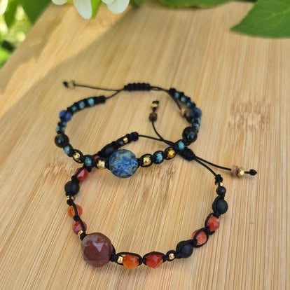 Two beaded bracelets with gemstone charms on a wooden surface with green foliage background