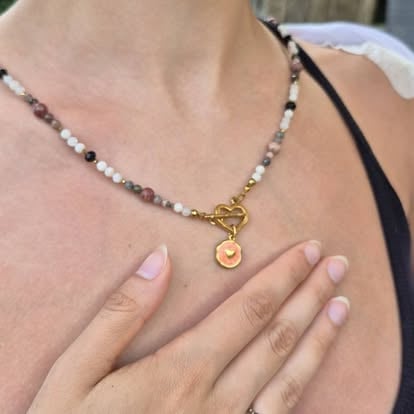 Person wearing beaded necklace with gold toggle clasp and small pendant charm